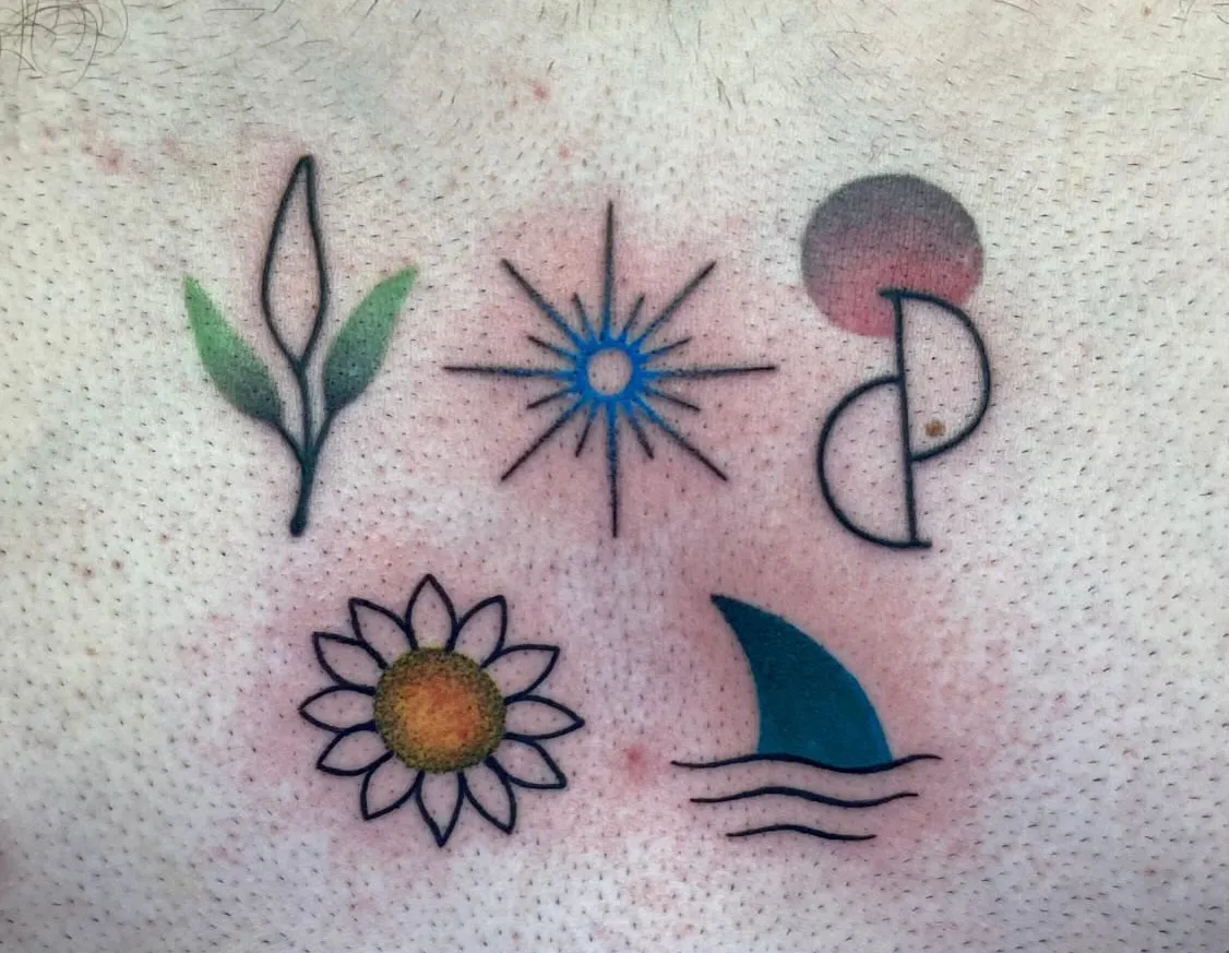 A small, minimalist tattoo on a person's chest featuring three simple symbols in a row: a green plant stem with leaves on the left, a blue starburst or sun design in the center, and a stylized red OptInk symbol. The tattoo area appears slightly reddened, suggesting it may be recently completed. The design is positioned centrally on the upper chest between areas of chest hair, with the symbols rendered in a clean, simple line art style with minimal color. Below, a flower and a shark fin.